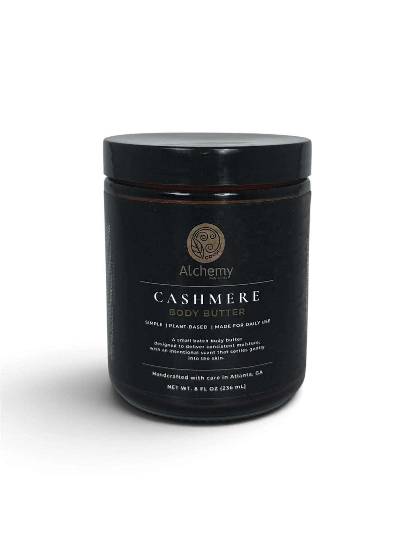 A amber jar with black lid and black label of Alchemy Cashmere Body Butters on a white background with a soft shadow.