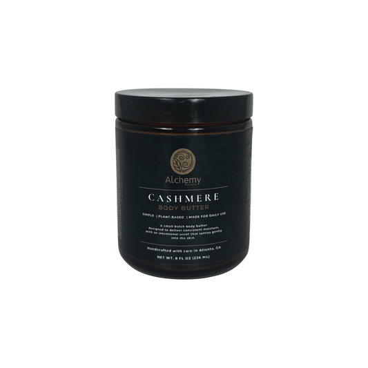 A amber jar with black lid and black label of Alchemy Cashmere Body Butters on a white background.