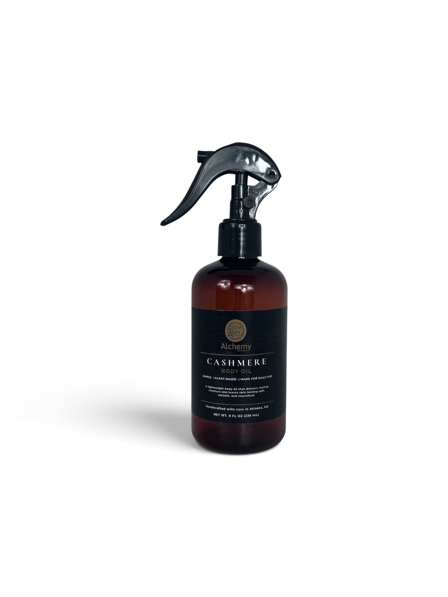 An amber spray bottle with a black trigger sprayer and a black label of Alchemy Body Werks Cashmere Body Oil on a clean white background.