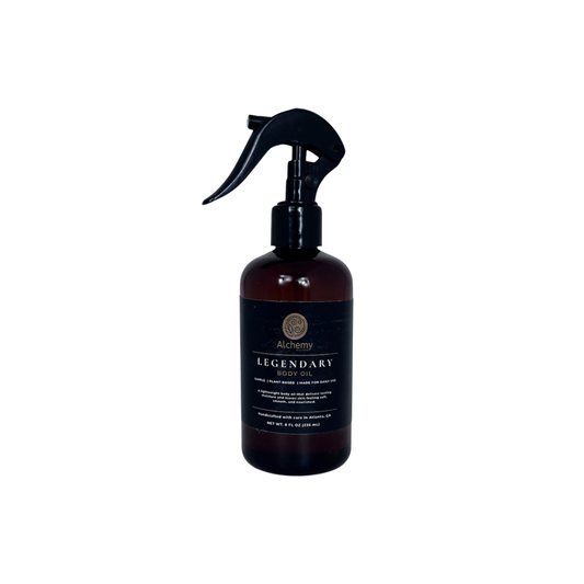 An amber spray bottle with a black trigger sprayer and a black label of Alchemy Body Werks Legendary Body Oil on a white background.
