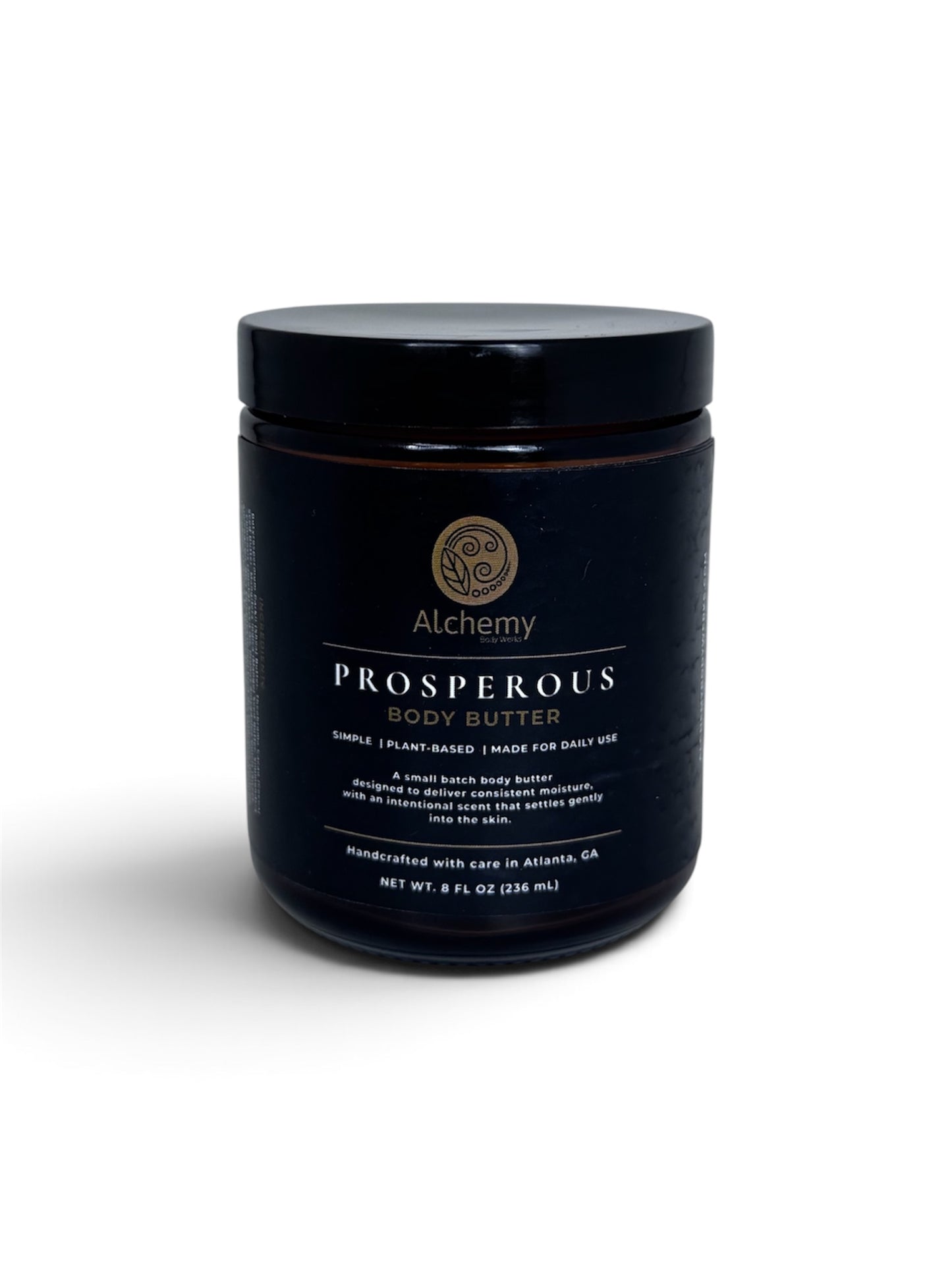 An amber jar with a black lid and black label of Alchemy Body Werls Prosperous Body Butter on a white background with a soft shadow.