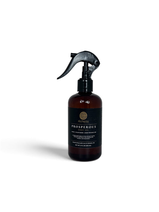 An amber spray bottle with a black trigger sprayer and a black label of Alchemy body Werks Prosperous Body Oil on a clean white background.