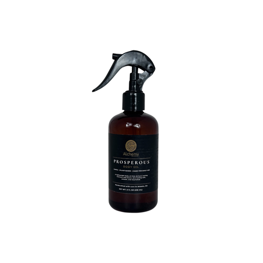 An amber spray bottle with a black trigger sprayer and a black label of Alchemy body Werks Prosperous Body Oil on a clean white background.