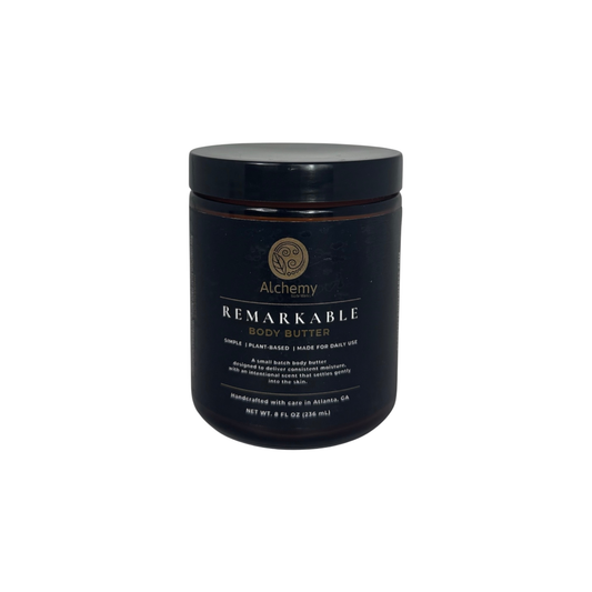 An amber jar with a black lid and black label of Alchemy Body Werks Remarkable Body Butter on a white background.