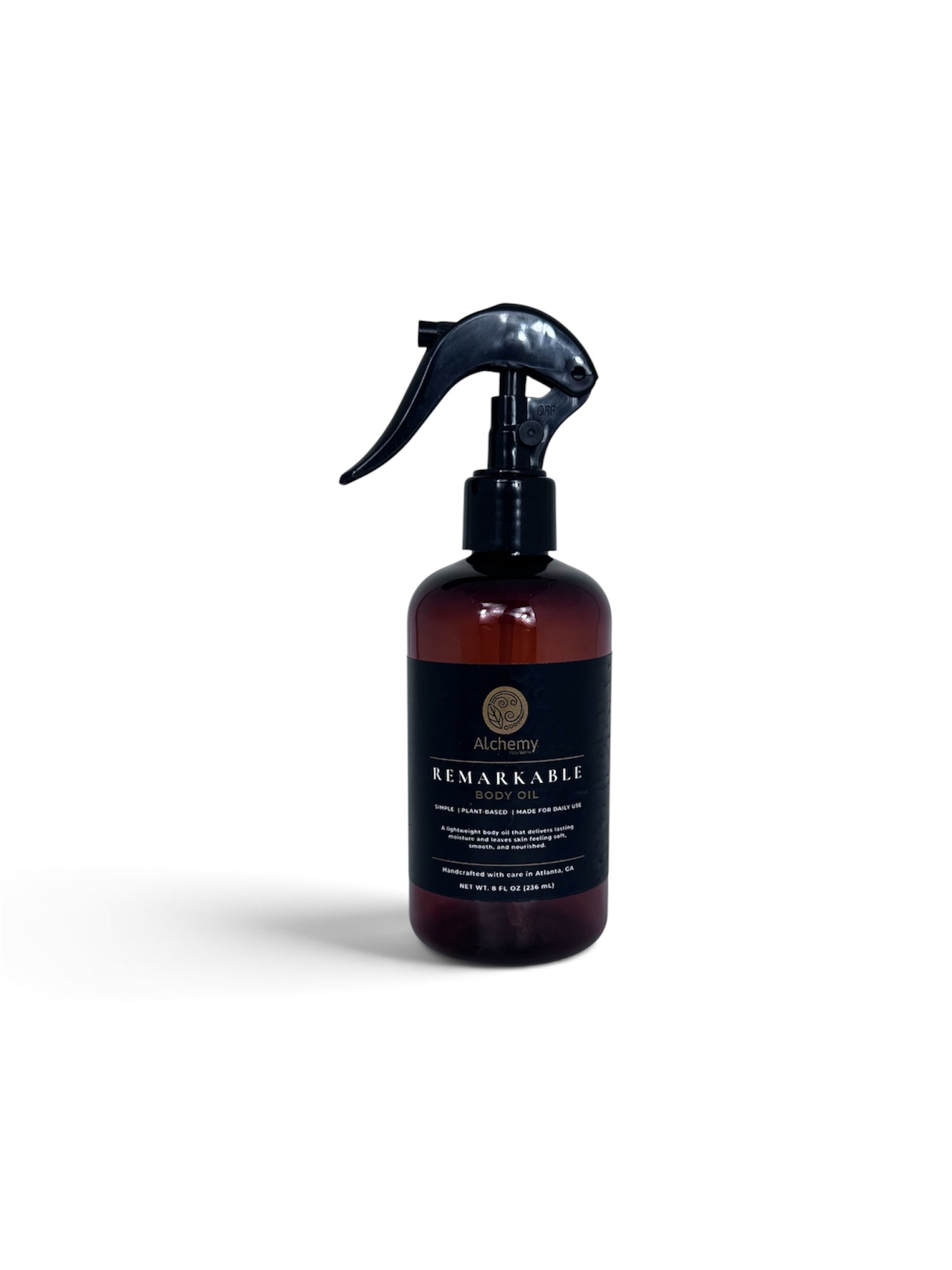 An amber bottle with black spray nozzle and black label of Alchemy Body Werks Remarkable Body oil with a soft white background.