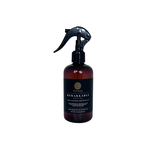 An amber bottle with black spray nozzle and black label of Alchemy Body Werks Remarkable Body oil with a white background.